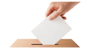 A hand entering a voting ballot into the ballot box.